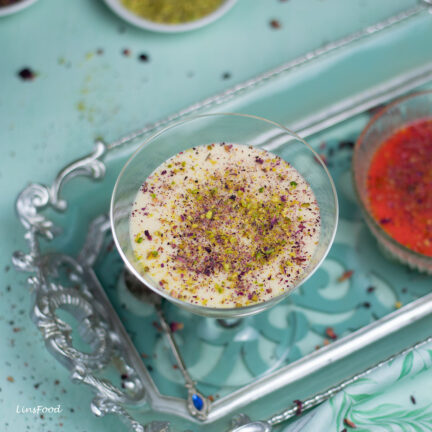 Muhallabia, middle eastern milk pudding, in a cocktails glass topped with crushed dried rose petals and pistachios